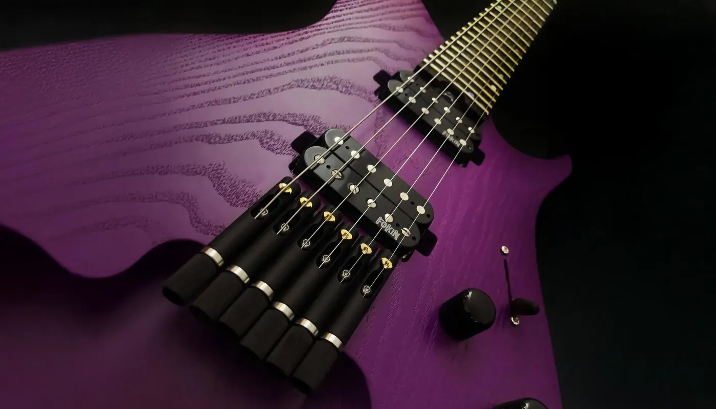 Six black TAN headless bridges with gold saddles on a purple ash guitar